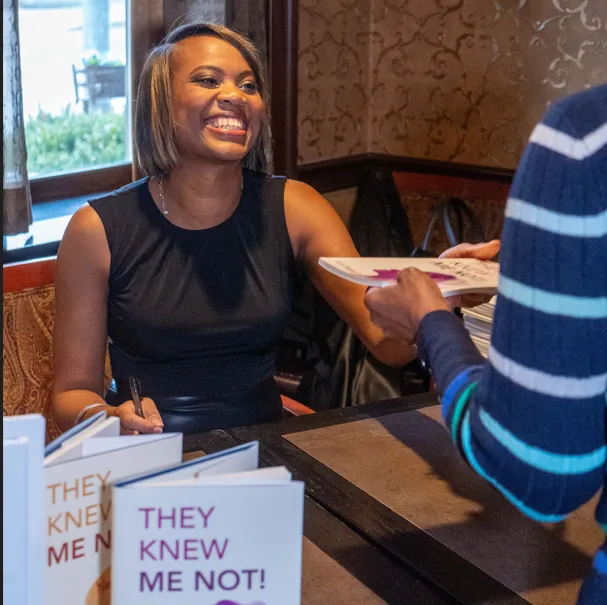 Rosa Allison signing copies of her book at a table stacked with them